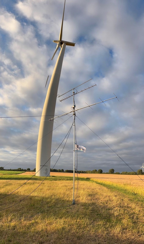 Der Antennenmast der Contestgruppe steht direkt neben einem Windrad auf einem Feld.