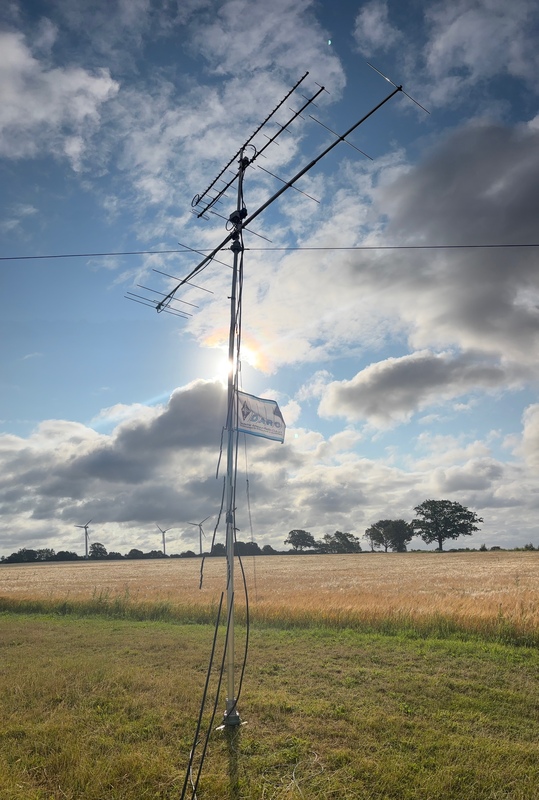 Der abgespannte Antennenmast mit mehreren Richtantennen und einer DARC-Flagge auf einem Feld.