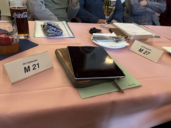 Getränke und Namensschilder stehen auf einem Tisch. Zentral liegt ein Tablet.