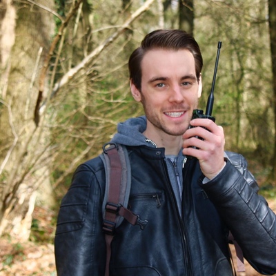 André steht mit Handfunkgerät in der Hand im Wald.
