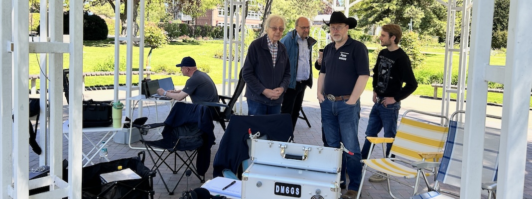 Fünf Personen im Musikpavillon; ein Operator arbeitet an der Amateurfunkstation.