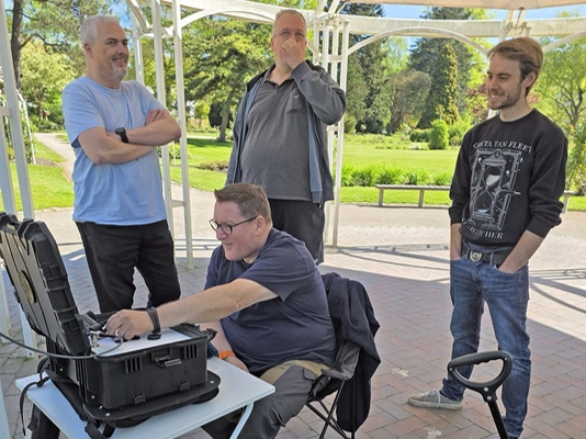 Vier Personen im Pavillon; ein Operator arbeitet am geöffneten Funkkoffer.