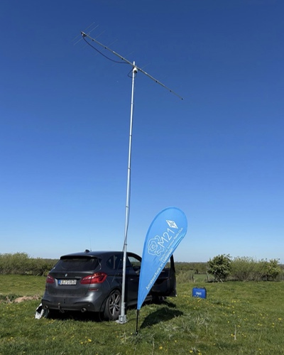 UKW-Yagi auf einem Mast am Auto befestigt, daneben steht eine Beachflag mit M21-Logo.