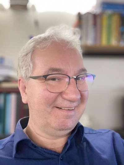 Lächelnder Mann mit Brille vor unscharfem Hintergrund.