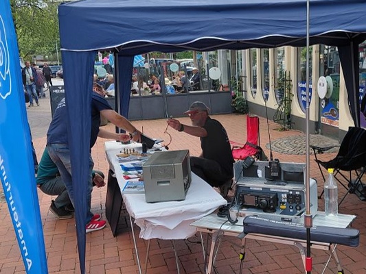 Blaues Faltzelt des M21-Stands mit Funkgeräten und Antenne in der Uetersener Fußgängerzone.